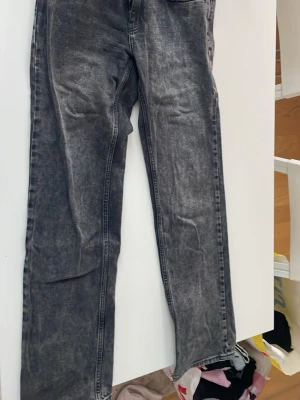 Mörkgrå raka jeans - Säljer ett par mörkgrå jeans med tvättad look och raka ben. Jeansen har klassisk femficksdesign och är tillverkade i jeansmaterial. Perfekt för dig som gillar en avslappnad och stilren vibe.