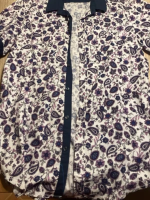 Blommig skjorta från Bruno Leoni - Säljer en skjorta från Bruno Leoni i storlek L med blommigt mönster i blått och lila på vit botten. Skjortan har mörkblå krage och knappslå, långa ärmar och är gjord i mjuk bomull med lite stretch. Perfekt för dig som gillar färg och mönster!