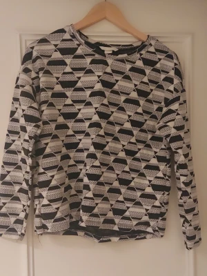 Svartvit mönstrad långärmad tröja S - Cool långärmad tröja i storlek S med svartvitt geometriskt mönster. Tröjan har rund hals och är tillverkad i ett mjukt stickat material som känns skönt mot huden. Perfekt för dig som gillar grafiska prints och vill ha något som sticker ut i garderoben.