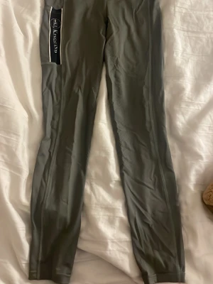 Kingsland ridbyxor i mörkgrönt  - Snygga mörkgrå ridbyxor från Kingsland med logga på benet. De är tillverkade i ett stretchigt syntetmaterial som ger bra passform och komfort vid ridning. Perfekta för dig som vill ha stil och funktion i stallet.