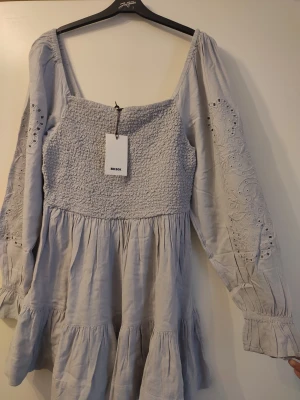Ljusgrå klänning i storlek M - Vacker ljusgrå klänning med fina detaljer. Helt ny, aldrig använd, med lappar kvar! Ord.pris 699kr.