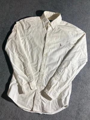 Vit skjorta från Ralph Lauren Slim Fit - Vit långärmad skjorta från Ralph Lauren i storlek M slim fit-modell. Klassisk krage, knappar hela vägen och broderad logga på bröstet. Skjortan är ändast använd vid ett tillfälle så alltså en helt ny skjorta👍✅ nypris:1200 mitt pris:549kr🤩 priset är aldrig hugget i sten🪨och det är bara att höra av dig om du har några funderingar🤗
