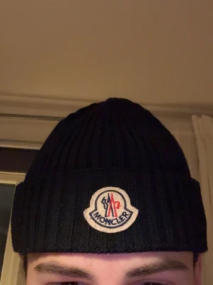 Moncler mössa - Svart ribbstickad mössa från Moncler med uppvikt kant och klassisk Moncler-logga framtill ⚫️⚪️.Mössan är tillverkad i mjukt material och har en enkel, stilren design som passar perfekt för kalla dagar. Nypris ca 2500kr! ✅🔥🙌