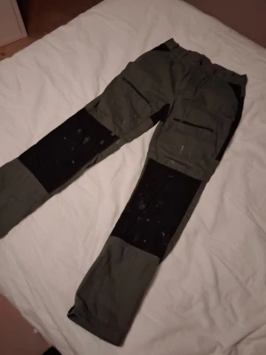 Gröna cargopants med svarta detaljer - Säljer ett par gröna cargopants med svarta förstärkningar på knän och bak i storlek 160. Den vänstra dragkedjan funkar ej.💕 Byxorna har flera fickor med dragkedja och är tillverkade i slitstarkt bomullsmaterial. Perfekta för dig som gillar funktionella och snygga byxor med utility-vibe.💕