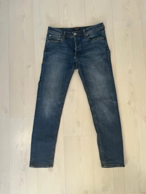 Jack & Jones Comfort/Mike jeans blå - Snygga blå jeans från Jack & Jones, modell Comfort/Mike. Klassisk femficksdesign med raka ben och normal passform. Jeansen har en mörkblå tvätt med lätt slitning och detaljerade sömmar. Perfekt för dig som gillar stilrena och bekväma jeans.