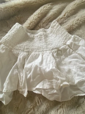 Vit volangkjol med smock - Supersöt vit kortkjol med bred smock i midjan och volangig nederdel från Zara. Kjolen är gjord i ett mjukt bomullstyg som känns lätt och luftig. Kan även användas som en topp 💕💕
