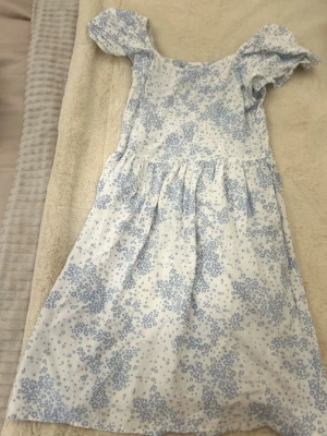 Vit och blå blommig kortklänning💕 - Söt kortklänning i vit bomull med ljusblå blommigt mönster. Klänningen är i storlek 158 och kommer från Kappahl. Endast använd 2 gånger🥰