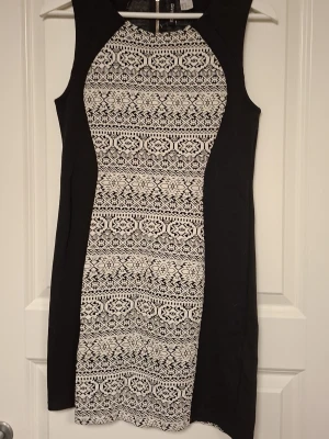 Svartvit mönstrad klänning H&M - Snygg svartvit klänning från H&M i storlek 40. Klänningen är ärmlös och har ett geometriskt mönster framtill och baktill, med svarta paneler längs sidorna. Kort modell med rund hals och dragkedja i ryggen. Perfekt för dig som gillar stilrena kontraster.