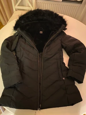 Svart pufferjacka med fuskpäls från Zara - Säljer en svart pufferjacka från Zara med fluffig fuskpäls i huvan och mjukt pälsfoder på insidan. Den är använd men är ändå i bra skick. 