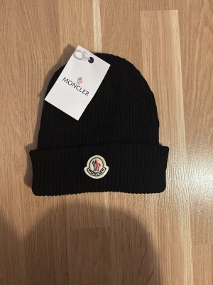 Svart Moncler mössa i ribbad ull - Hej säljer en helt ny svart Moncler mössa, priset är diskuterbart.