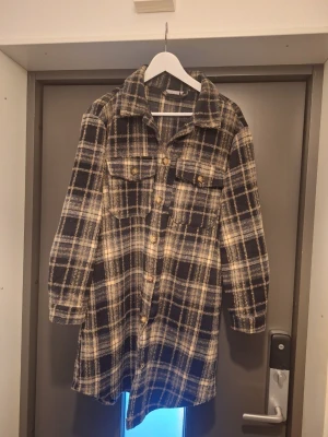 Rutig overshirt från Fransa stl L - Lång, rutig overshirt/kappa i mörkblått och beige med stora bröstfickor och knappar framtill. Skön och avslappnad passform, perfekt att slänga över en hoodie eller t-shirt. Nypris 1250:-