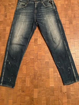 Replay Sandot  jeans - Säljer ett par Replay Sandot jeans i relaxed tapered fit. De är mörkblå med slitningar och vita färgstänk för en cool, streetad look. Klassisk femficksmodell med Replay-logga på fickan och snygga detaljer på bakfickorna. Materialet är jeans i bomull. Väldigt varsamt används ett fåtal gånger, i princip nyskick.  Nypris 1800 || storlek 30/30 men skulle säga att de passar som 32/30 ungefär, de är väldigt stretchiga. 