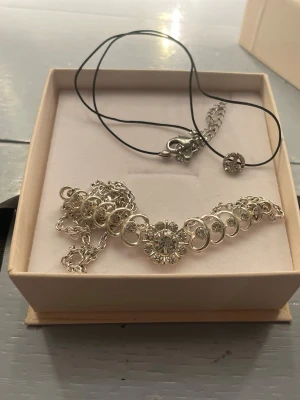 Två halsband  - Säljer ett set med ett silverfärgat halsband med gnistrande stenar och cirkeldetaljer samt ett svart halsband med en liten glittrig berlock. Kontakta ifall du är intresserad av ett av halsbanden istället för båda🤍