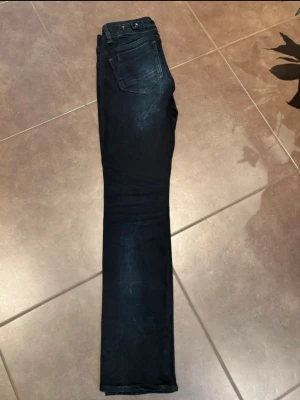 G-Star RAW Midge Mid Straight jeans - Snygga mörkblå jeans från G-Star RAW, modell Midge Saddle Mid Straight. Klassisk femficksdesign med raka ben och subtila slitningar framtill. Jeansen har midja med bälteshällor och metallknappar. Perfekta för dig som gillar en clean och tidlös look. Innerben: 77cm Ytterben: 101cm