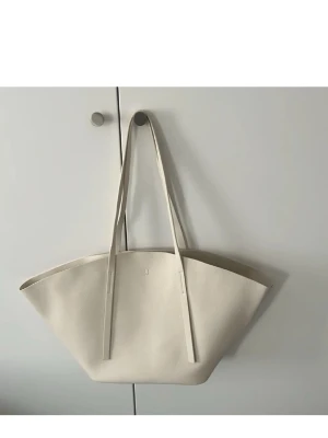 Beige shoppingväska från Gina Tricot  - Säljer en stilren och rymlig shoppingväska från Gina Tricot i beige skinn. Väskan har en modern, bred form med långa axelband och minimalistisk design. Insidan är enkel med en liten D-ring för nycklar eller accessoarer. Perfekt för dig som gillar clean och snygg look. Ordinarie 599kr pris 250kr