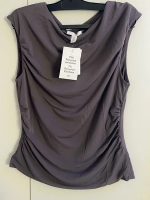 Mörkgrå draperad topp från H&M - Säljer en mörkgrå, ärmlös topp från H&M 