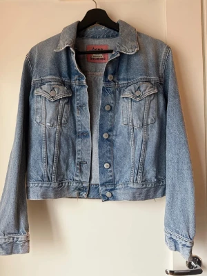 Jeansjacka från Acne Studios Blå Konst - Säljer en klassisk ljusblå jeansjacka från Acne Studios Blå Konst. Jackan har raka linjer, två bröstfickor med lock och knappar framtill. Tillverkad i 100% bomull och har en snygg, tidlös look som funkar året runt.