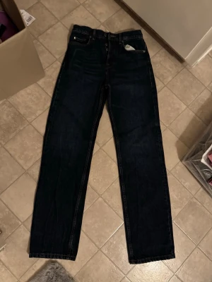 Mörkblå raka jeans från Zara - Säljer ett par mörkblå jeans från Zara med klassisk femficksmodell och raka ben. Jeansen har hög midja och är tillverkade i kraftig bomullsdenim. Snygga kontrastsömmar och enkel design som passar till allt. Perfekta för dig som gillar en clean och tidlös look.