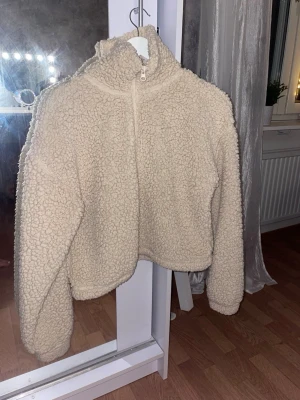 Beige teddytröja från Bik Bok XS - Supermysig teddytröja i beige från Bik Bok, storlek XS. Tröjan har hög krage, halv dragkedja och fluffigt material som ger en chill vibe. Perfekt för kalla dagar när du vill vara både varm och snygg. Passar dig som gillar en loose fit och vill ha en tröja som sticker ut. 🤗