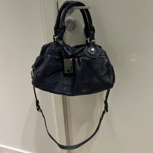 Marc Jacobs väska mörkblå - Jätte fin väska från marc jacobs i mörkblå med silvriga detaljer, väldigt bra skick endast lite sliten, som undersidan på silver detaljerna och nån pytte liten fläck inuti men verkligen inget som märks! Dustbagen finns och även långa bandet!