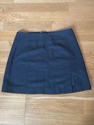 Mörkgrå kortkjol från Monki m slit - Säljer en stilren mörkblå kortkjol från Monki i storlek 34. Kjolen har en rak passform med diskret slits framtill och dragkedja bak. Materialet är en mix av polyester, viskos och elastan som ger en mjuk och följsam känsla. Perfekt för dig som gillar minimalistisk och clean look.