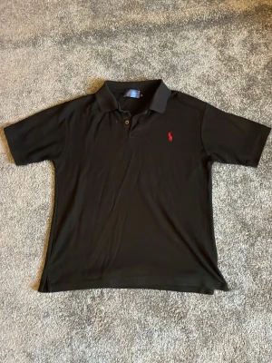 Svart pikétröja från Polo Ralph Lauren - Säljer en Svart Ralph lauren piké i utmärkt skick. Storleken är M. Säljer billigt då jag vill bli av med kläderna i min garderob. Priset är inte satt i sten så kom med bud!  KOLLA IN MIN PROFIL FÖR KLÄDER TILL ETT BARNSLIGT PRIS 🏆 