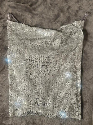 Glittrig silver paljettopp från Zara - Säljer en snygg glittrig silverfärgad paljettopp från Zara med tunna axelband. Toppen har en rak passform och är perfekt för att sticka ut på festen. Materialet är täckt av paljetter som ger ett riktigt coolt skimmer.