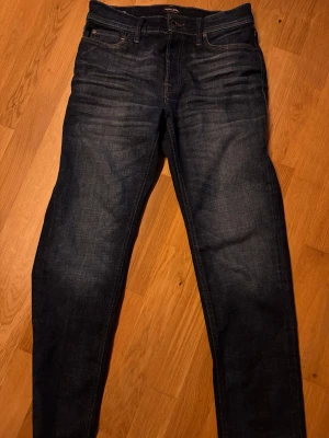 Jack & Jones mörkblå tapered jeans 29/32 - Säljer ett par mörkblå jeans från Jack & Jones, modell Tapered/Mike. Jeansen har klassisk femficksdesign, snygga slitningar och kontrastsömmar. Passformen är tapered vilket ger en smalare siluett nedtill. Perfekta till sneakers eller boots.