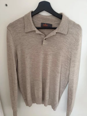Beige pikétröja i merinoull från Morris - Snygg beige pikétröja från Morris i 100% merinoull. Tröjan har klassisk krage, två knappar vid halsen och långa ärmar. Perfekt för dig som gillar stilrena och mjuka plagg med lite lyxig känsla. Passar dig som vill ha en enkel men ändå elegant look. Den är lite lite på mig jag är 183 cm