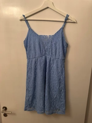 Ljusblå spetsklänning med smala axelband - Superfin ljusblå klänning med smala axelband och v-ringning. Klänningen är täckt av ett vackert spetsmönster och har en kort längd som känns både söt och trendig. Perfekt för sommarens alla tillfällen!