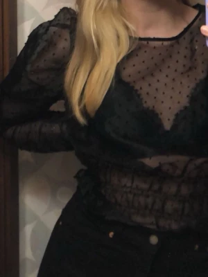 Svart transparent prickig blus - Säljer en svart transparent blus med långa puffärmar och små prickar över hela tyget. Blusen är croppad med resår i midjan och har en rund halsringning. Jag har tyvärr klippt bort lappen där man ser storlek och märke (den syntes för mycket när man hade den på sig), men jag skulle gissa att den är i storlek M.