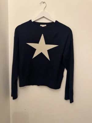 Mörkblå tröja med stjärna Gina Tricot - Mysig mörkblå tröja från Gina Tricot med en stor vit stjärna på bröstet. Klassisk rund halsringning och långa ärmar. Perfekt för dig som vill ha en enkel men ändå statement vardagströja.