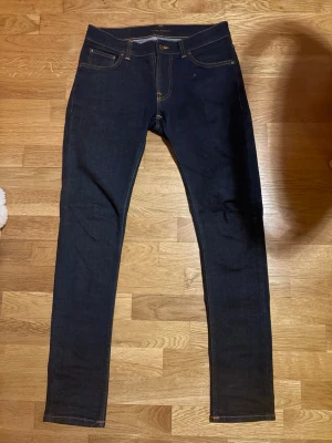 Tight Terry Jeans Nudie - Marinblå Nudie jeansen från Nudie. Jeansen har smal passform. Nudie-logga på bakfickan och läderpatch i midjan. Modellen är 180 cm.
