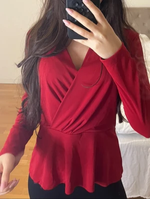 Röd omlottopp från H&M - Röd omlottopp från H&M i mjukt material. Toppen har lång ärm, markerad midja och en snygg v-ringning. Säljer pga rensning. 