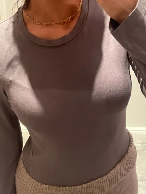 Grå långärmad body topp  - Säljer en enkel och stilren grå långärmad topp med rund hals. Toppen är i mjukt bomullsmaterial och har en tight passform som sitter snyggt mot kroppen. Perfekt att matcha med både jeans och kjol för en clean look.