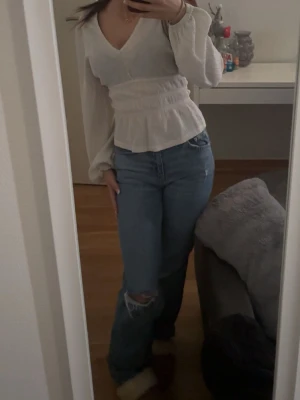 Blå jeans med hål på knät - Säljer ett par blå jeans med klassisk femficksdesign och ett snyggt hål på ena knät för en avslappnad vibe. Jeansen har rak passform och normal midja, perfekta till en chill outfit. Materialet är jeans och färgen är en mellanblå ton.