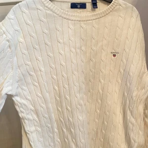 Vit tröja från GANT - Vit tröja från GANT med broderad logga på bröstet. Klassisk rund halsringning och ribbade muddar. Perfekt för dig som gillar en clean och tidlös stil. Skön och mjuk känsla tack vare det stickade materialet. Storlek är 170 cm (15 år) men passar både S och M.