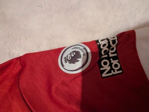 Liverpool M. Salah 11 matchtröja - Riktigt snygg Liverpool FC matchtröja med M. Salah och nummer 11 på ryggen. Röd med vita detaljer, broderat klubbmärke och FIFA World Champions 2023-emblem. Premier League-patch på ärmen och Standard Chartered tryck på bröstet. Perfekt för fotbollsfans!