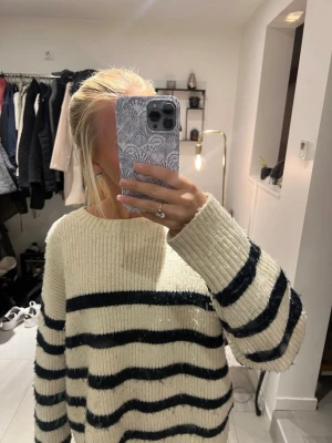 Randig stickad tröja i offwhite - Mysig stickad tröja i offwhite med breda svarta horisontella ränder. Tröjan har en rund halsringning och långa ärmar med loose passform. Ribbstickad struktur som ger en chill och avslappnad vibe, perfekt för lager på lager under kyliga dagar. Går nt att köpa längre!!!