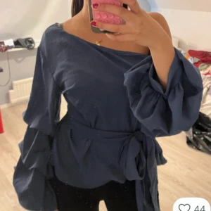 Mörkblå offshoulder blus med volangärm - Snygg mörkblå blus med offshoulder-design och långa volangärmar. Blusen har ett knytband i midjan som ger en fin siluett och extra stilpoäng. Jätte fin , classy topp med fina volanger . Perfekt till vardags och på fest. Använd fåtal, max 3 gånger  Nypris 400kr! öppen för sänkning