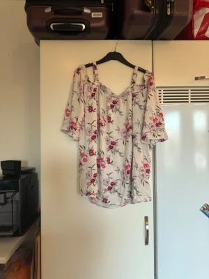 Blommig offshoulder blus från mywear - Säljer en ljusbeige blommig blus från mywear i storlek XL. Blusen har offshoulder-design med breda axelband och trekvartsärmar. Mönstret består av rosa och röda blommor med gröna blad. Materialet är mjukt och luftigt, perfekt för varma dagar. Storlek XL. Mycket fint skick, jag hittar inga synliga anmärkningar eller defekter. 