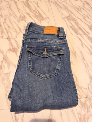Gina Tricot Jeans strl 32 - Blåa jeans från Gina med bootcut. Jeansen har normal passform, dragkedja och knapp framtill samt en bakficka med lock och knapp. Materialet är mjukt jeans-tyg med lite stretch. Säljer för att dom är för korta för mig, jag är 175 cm. 