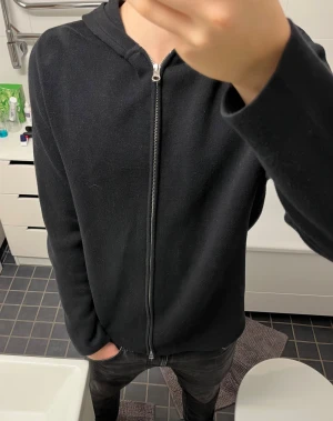 Svart hoodie med dragkedja från Samsøe - Svart hoodie från Samsøe Samsøe med hel dragkedja framtill och huva. Tröjan är stickad och har en clean passform . Perfekt för chill dagar och enkel att matcha. Materialet är bomull/Merino ull. Pris går att diskutera
