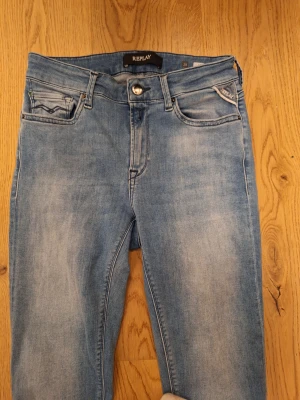 Replay ljusblå jeans, storlek 28 - Snygga ljusblå jeans från Replay med klassisk femficksdesign och diskret Replay-logga på fickan. Jeansen har en normal passform och raka ben, tillverkade i mjukt jeanstyg med lätt tvättad look. Perfekta för dig som gillar stilrena och bekväma jeans.