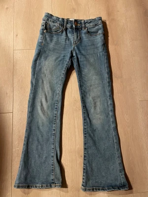 Blå bootcut jeans från 157 - Snygga blå jeans från 157 med klassisk femficksdesign och bootcut-ben. Jeansen har en normal passform och är tillverkade i slitstarkt denim med ljus tvätt och kontrastsömmar. Perfekt för dig som gillar retrovibbar och vill ha ett par jeans med lite extra sväng i benen.