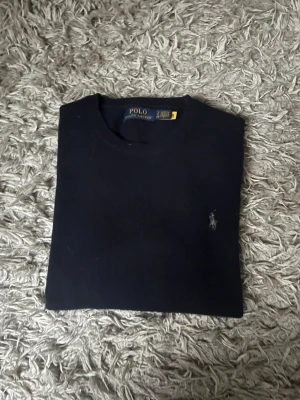 Mörkblå stickad navy wool tröja Polo Ralph Lauren - Snygg mörkblå stickad tröja från Polo Ralph Lauren med klassisk rund hals och diskret broderad logga på bröstet. Det är en stickad wool tröja som aldrig använts. Den är alltså i ett helt nytt skick. Storlek S.