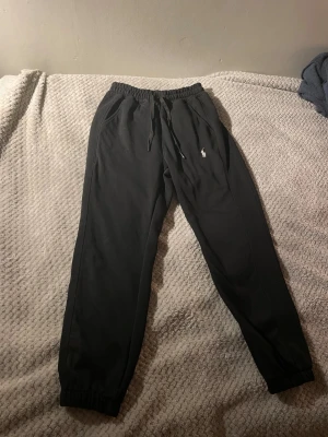 Polo Ralph Lauren byxor - Svarta mjukisbyxor från Polo Ralph Lauren med broderad logga på vänster ben. Byxorna har elastisk midja med snörning, ribbade muddar vid benslut och är gjorda i mjukt bomullsmaterial. Perfekta för chill eller streetwear.