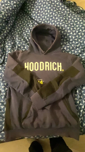 Svart hoodie från Hoodrich med tryck - Säljer en svart hoodie från Hoodrich med stor gul logga på bröstet och coolt världskarta-tryck på ryggen. Tröjan har huva, lång ärm och paneler i mörkare svart på ärmar och nedre delen. Perfekt för dig som gillar streetwear och snygga detaljer.