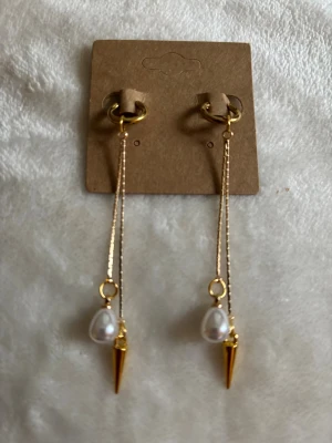Guldiga örhängen med pärlor och spikes - Snygga örhängen i guldfärgad metall med tunna kedjor, droppformade vita pärlor och coola guldfärgade spikes. Perfekt accessoar för att lyfta din look med både elegans och edge. Passar dig som gillar att sticka ut med detaljer.