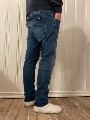 Blåa dondup jeans - Snygga blå jeans från Dondup med tapered passform och klassiska fem fickor. Jeansen har en mörk tvätt med lätt slitning och detaljerad med den  klassiska dondup loggan på bakfickorna. Perfekt för dig som gillar en modern och avslappnad stil.